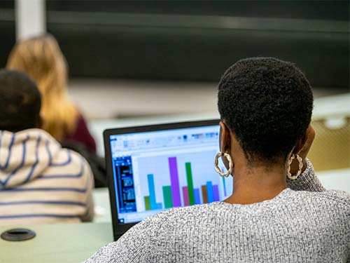 a student working on a laptop with multicolored bar charts displayed on screen